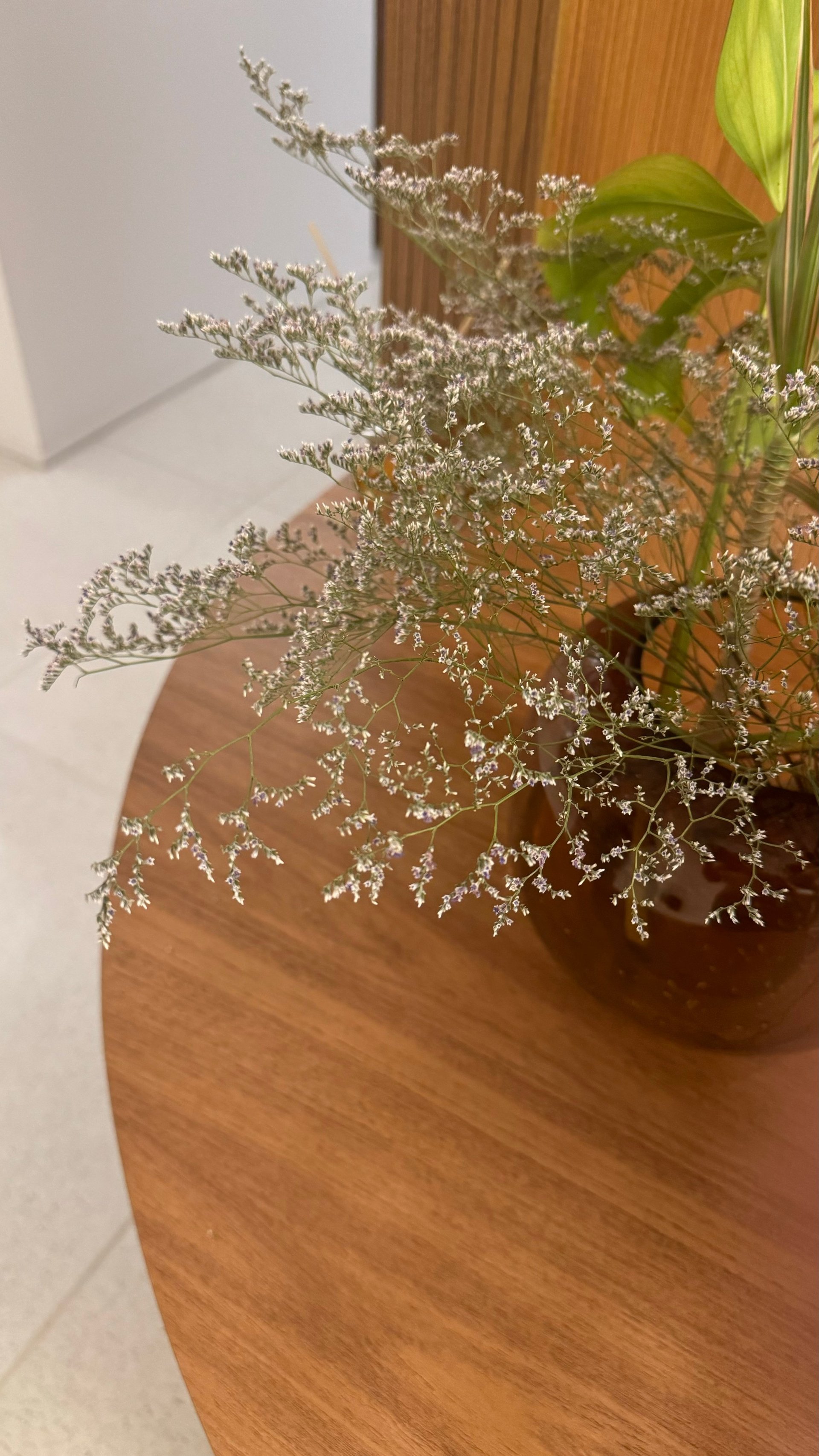 Wooden vase with delicate white babys breath flowers and green foliage on a table beside a white wall